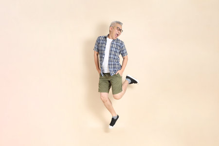 Portrait of an Asian senior man in glasses, Jumping, wearing casual plaid shirt, shorts, and...