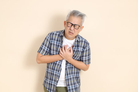 Portrait of an Asian senior man in glasses, wearing casual plaid shirt, shorts, and sneakers, isolated on beige background. Elderly male lifestyle concept.の写真素材