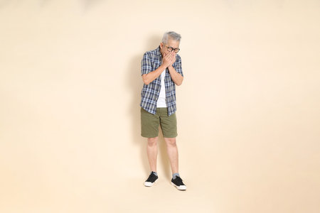 Portrait of an Asian senior man in glasses, wearing casual plaid shirt, shorts, and sneakers,...