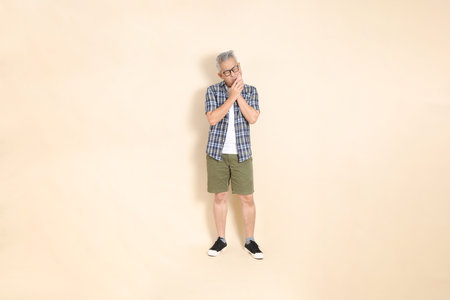 Portrait of an Asian senior man in glasses, wearing casual plaid shirt, shorts, and sneakers,...