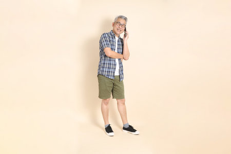 Portrait of an Asian senior man in glasses, Holding mobile phone, wearing casual plaid shirt,...