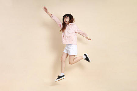 Young Asian woman wearing a pink UV protection hoodie jacket Jumping against a beige background, sun protection clothing concept.の写真素材