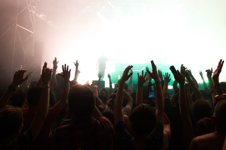 Stage lights and crowd of audience with hands raised at a music festival. Fans enjoying the party...