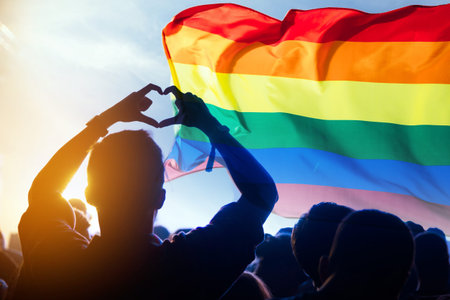 Pride community at a parade with hands raised and the LGBT flag.