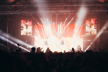 Stage lights and crowd of audience with hands raised at a music festival. Fans enjoying the party vibes.の写真素材