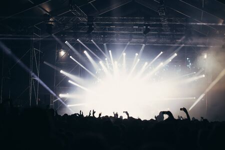 Stage lights and crowd of audience with hands raised at a music festival. Fans enjoying the party vibes.の写真素材