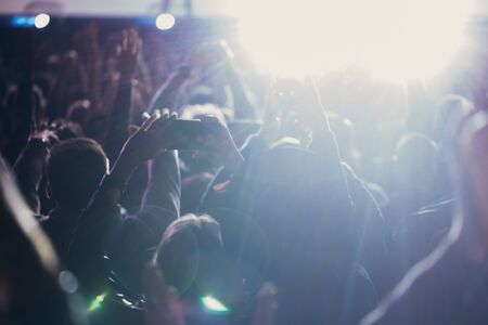 Stage lights and crowd of audience with hands raised at a music festival. Fans enjoying the party vibes.の写真素材