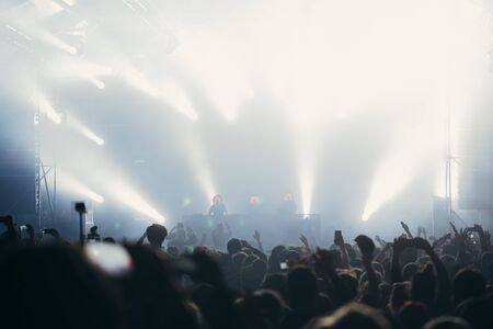 Stage lights and crowd of audience with hands raised at a music festival. Fans enjoying the party vibes.の写真素材