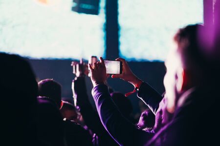 Stage lights and crowd of audience with hands raised at a music festival. Fans enjoying the party vibes.の写真素材