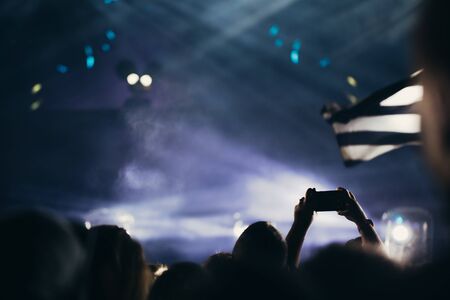 Stage lights and crowd of audience with hands raised at a music festival. Fans enjoying the party vibes.の写真素材