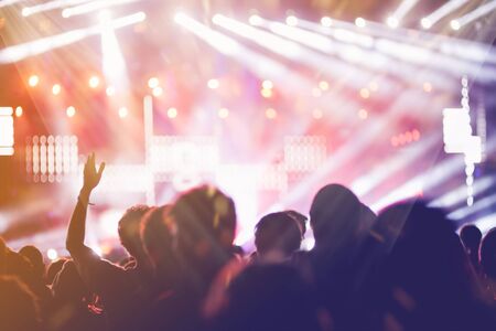 Stage lights and crowd of audience with hands raised at a music festival. Fans enjoying the party vibes.の写真素材