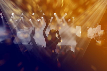 Stage lights and crowd of audience with hands raised at a music festival. Fans enjoying the party...