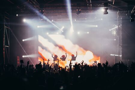 Stage lights and crowd of audience with hands raised at a music festival. Fans enjoying the party vibes.の写真素材