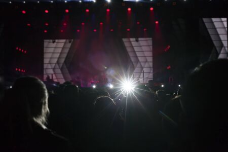 Stage lights and crowd of audience with hands raised at a music festival. Fans enjoying the party vibes.の写真素材