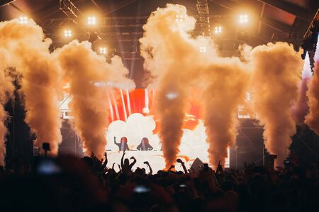 Stage lights and crowd of audience with hands raised at a music festival. Fans enjoying the party vibes.の写真素材