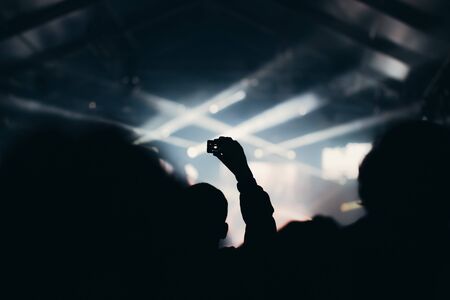 Stage lights and crowd of audience with hands raised at a music festival. Fans enjoying the party vibes.の写真素材