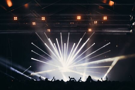 Stage lights and crowd of audience with hands raised at a music festival. Fans enjoying the party vibes.の写真素材