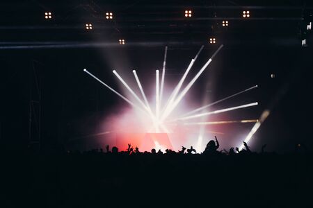 Stage lights and crowd of audience with hands raised at a music festival. Fans enjoying the party vibes.の写真素材