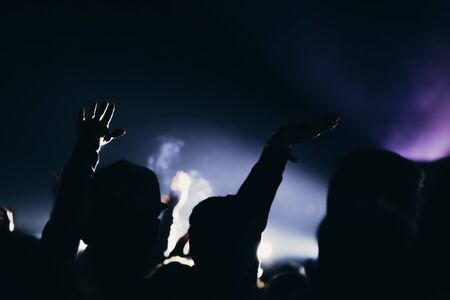 Stage lights and crowd of audience with hands raised at a music festival. Fans enjoying the party vibes.の写真素材