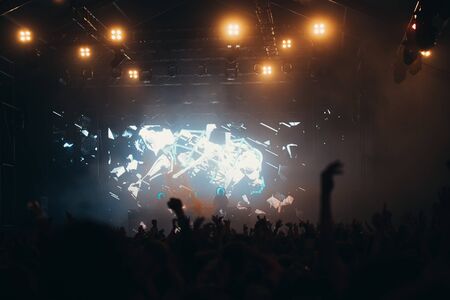 Stage lights and crowd of audience with hands raised at a music festival. Fans enjoying the party vibes.の写真素材
