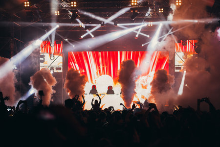 Stage lights and crowd of audience with hands raised at a music festival. Fans enjoying the party...