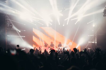 Stage lights and crowd of audience with hands raised at a music festival. Fans enjoying the party vibes.の写真素材