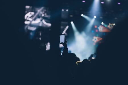 Stage lights and crowd of audience with hands raised at a music festival. Fans enjoying the party vibes.の写真素材