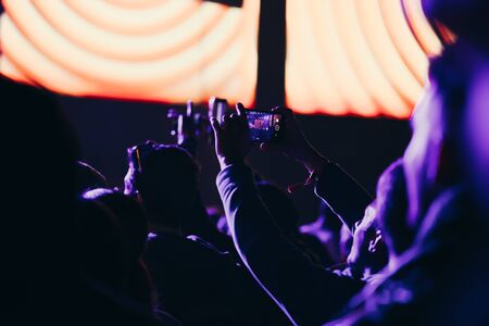 Stage lights and crowd of audience with hands raised at a music festival. Fans enjoying the party vibes.の写真素材