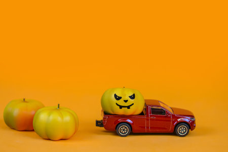 Halloween pumpkins and red car on orange background with copy space