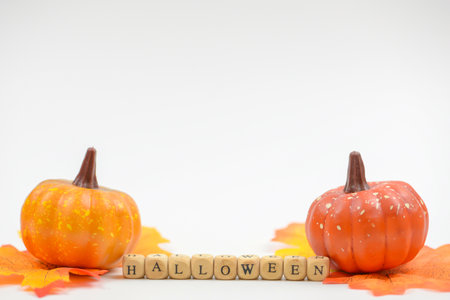 Halloween pumpkins with fall leaves and wooden cubes on white backgroundの写真素材