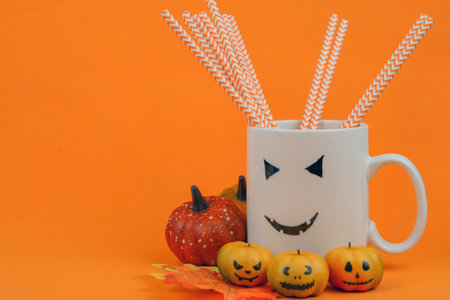 Halloween pumpkins and drinking straws in cup on orange backgroundの写真素材