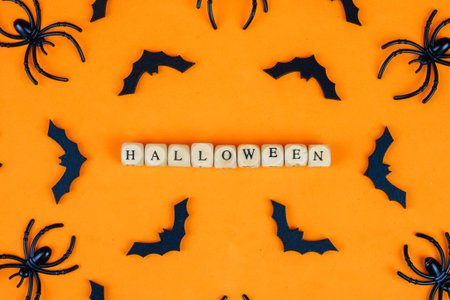 Halloween concept with black bats and wooden cubes with letters on orange background