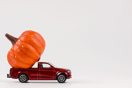 Miniature red toy car with pumpkins on a white background.