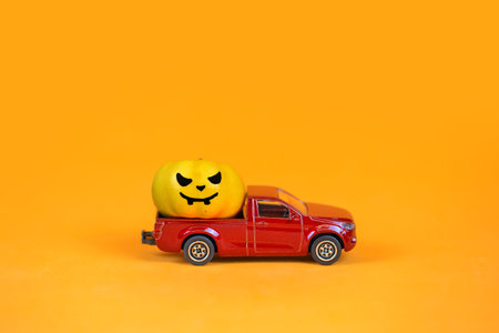 Halloween pumpkin on a red car on orange background. Halloween concept.の写真素材