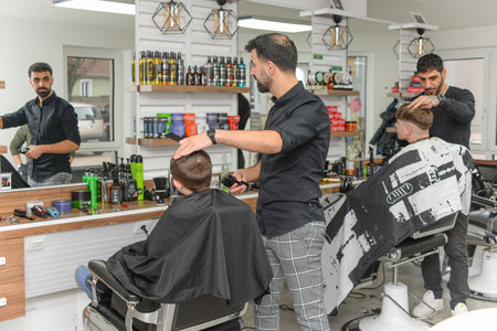 Hairdresser cuts hair of young man in barbershopの写真素材