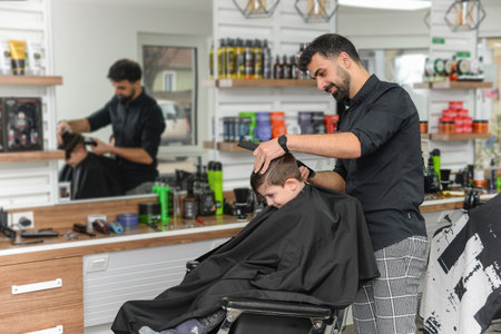 Hairdresser cutting hair of young man in barbershopの写真素材
