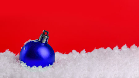 Blue Christmas ball in the snow on a red background with copy spaceの写真素材