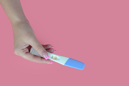Female hand holding a positive pregnancy test isolated on a pink background.