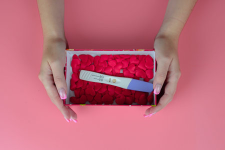 Female hands holding a pregnancy test in a box of red rose petals