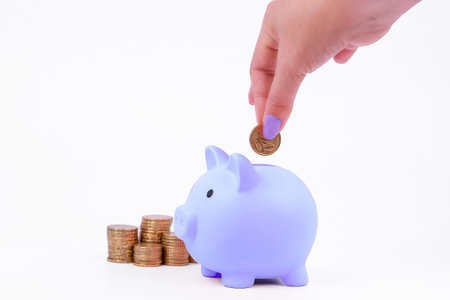 Female hand putting coin into piggy bank, isolated on white backgroundの写真素材