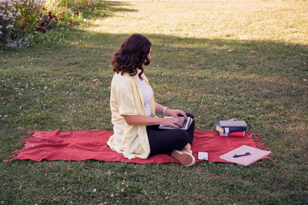 Young woman with laptop and books in park studying