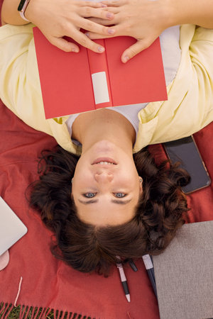 Young woman lying on grass with phone and books, top view