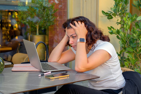 Young woman freelancer working with laptop at terrace table and talking on phone