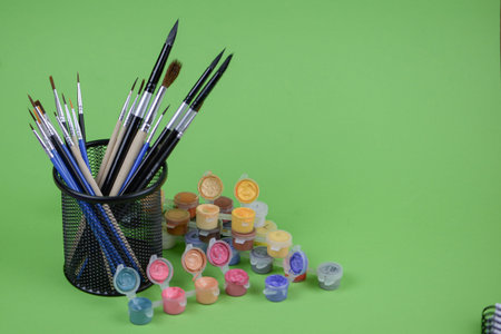A cup that is filled to the brim with various paint brushes and a collection of colorful bottles of...