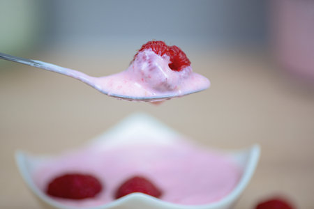 A closeup view of creamy raspberry yogurt elegantly placed on a spoon, beautifully topped with fresh raspberriesの写真素材