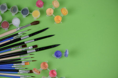 A collection of various paint brushes alongside numerous bottles of vibrant paint set against a beautiful green backgroundの写真素材