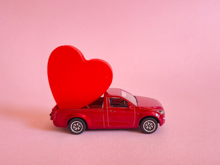 A vibrant red toy car featuring a lovely red heart placed in the back of the vehicle, all set against a soft pink backgroundの写真素材