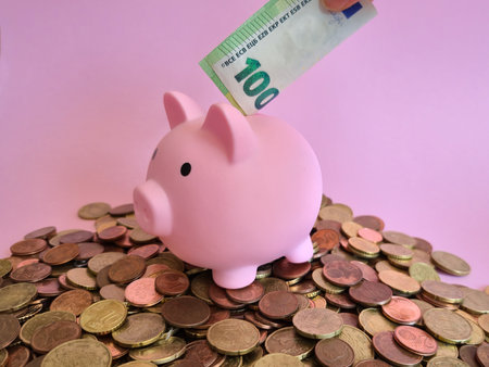 A delightful pink piggy bank displaying a 100 euro bill that is sticking out of the top, symbolizing saving money effectively and joyfullyの写真素材
