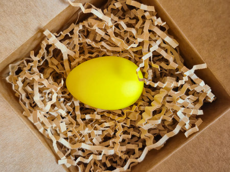 A bright yellow egg is carefully placed within a box that is filled with crumpled and shredded pieces of paper for cushioningの写真素材