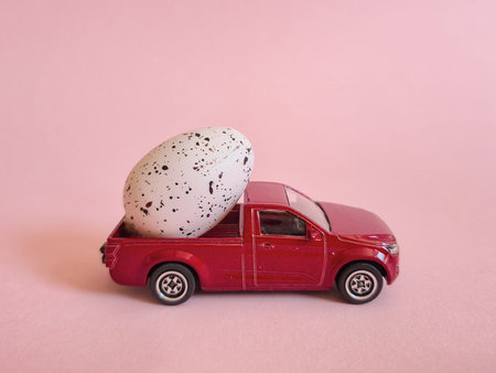 A colorful toy truck carrying an egg in its cargo area placed on a vibrant pink background, creating a visually appealing sceneの写真素材
